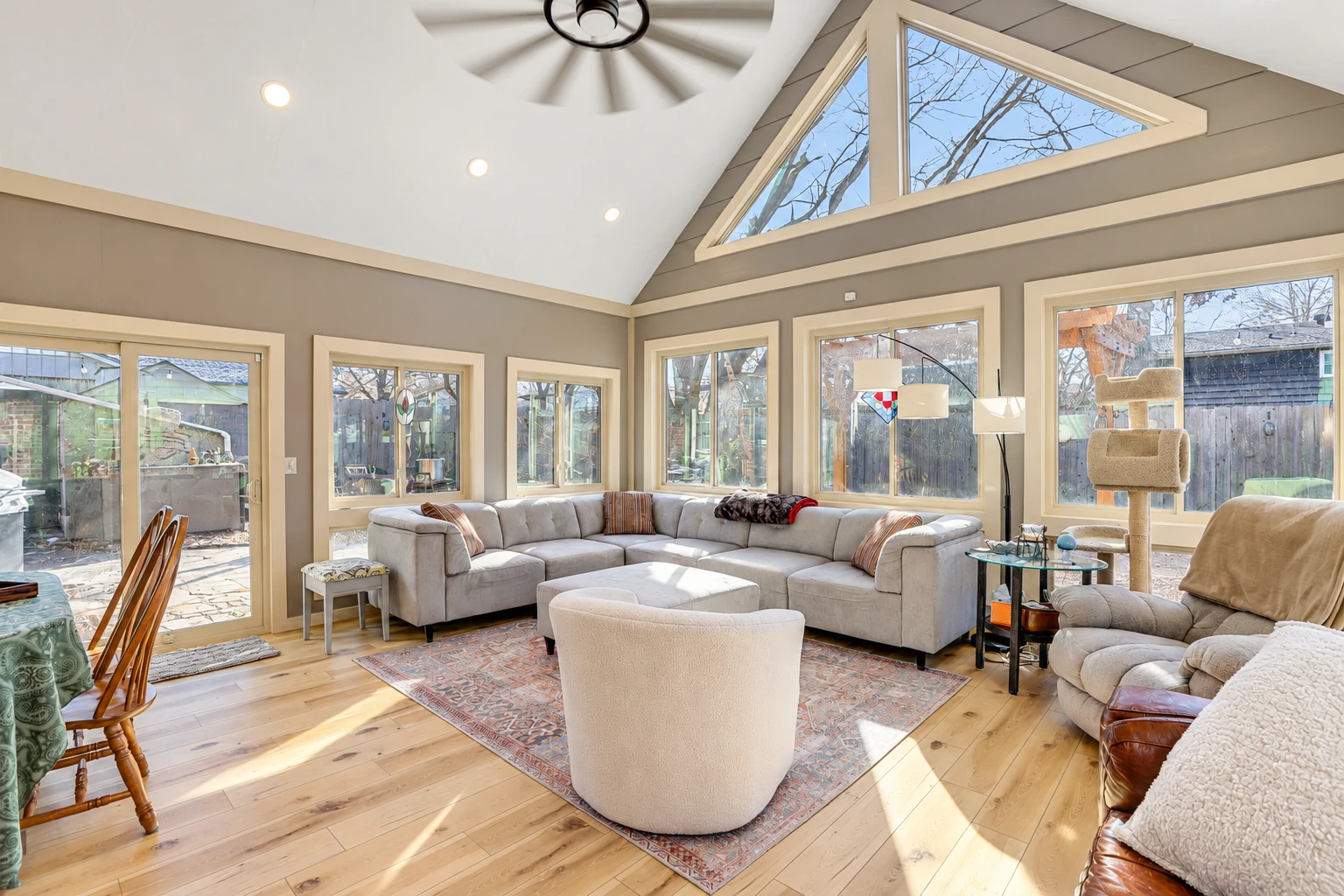 A bright four-season sunroom with a vaulted ceiling, large windows, and a sectional sofa around a rug.