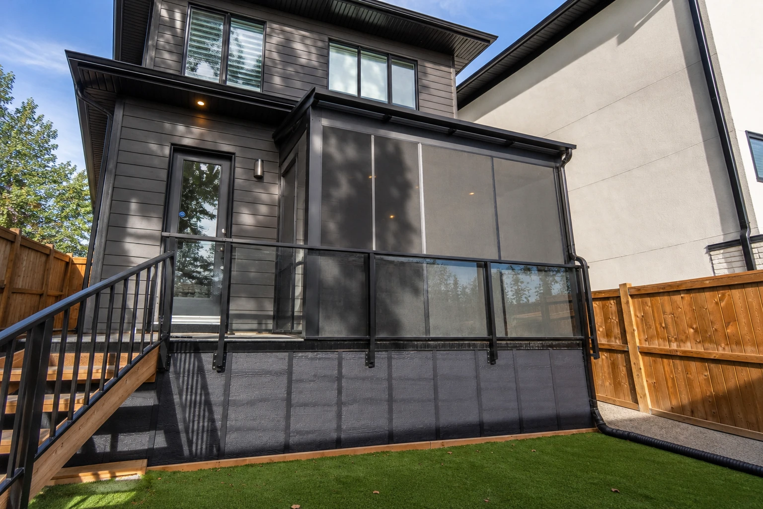 Raised deck with a dark patio cover and screened sides, attached to a modern house.