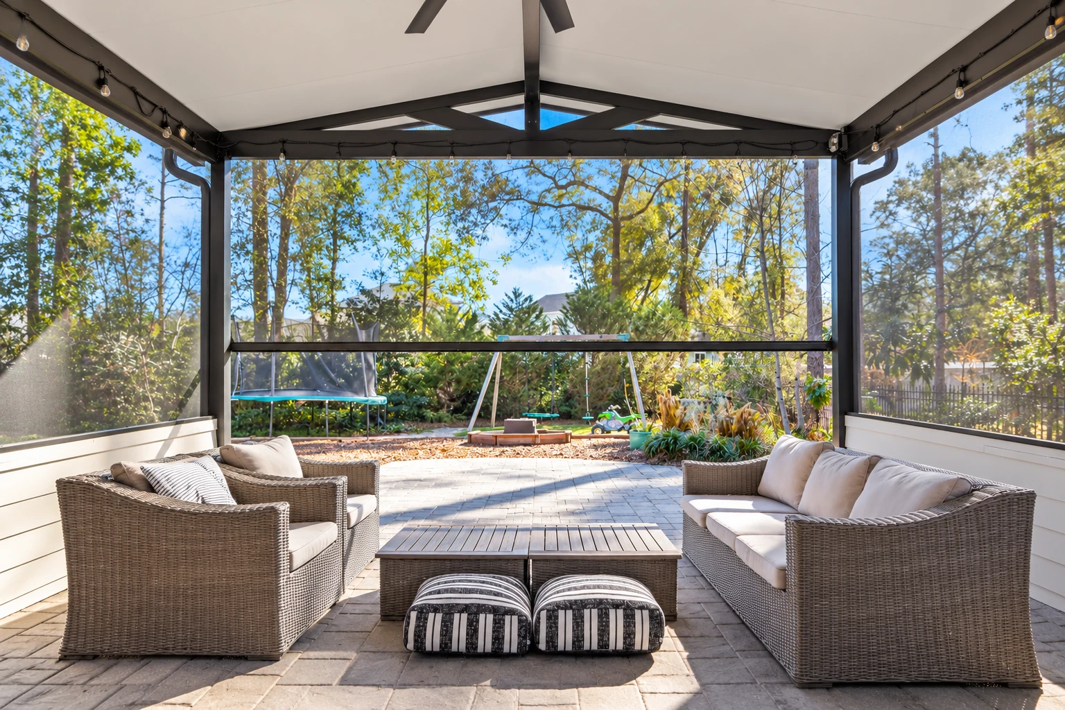 Screened patio enclosure with a peaked white roof, wicker seating, and views of the garden.