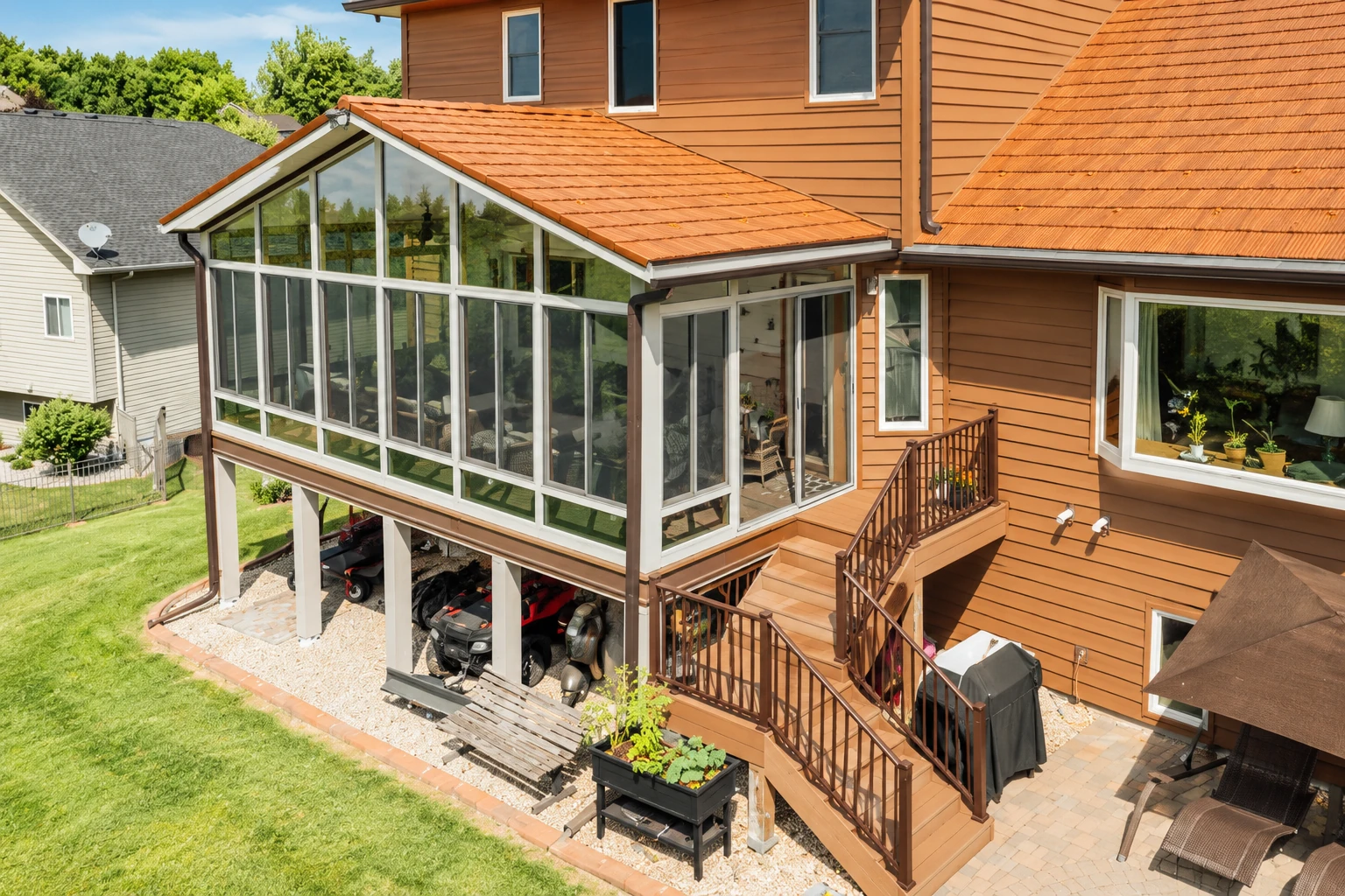 Raised sunroom addition with a terracotta-tiled roof and large white-framed windows attached to a brown house.