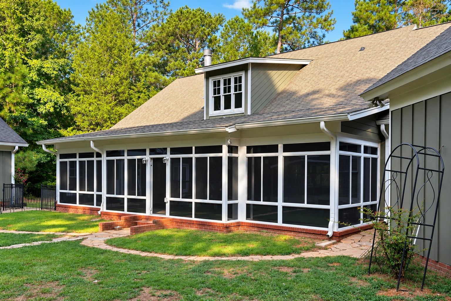 A white-framed screen room addition spans the back of a house, set on a brick base beneath a shingled roof.