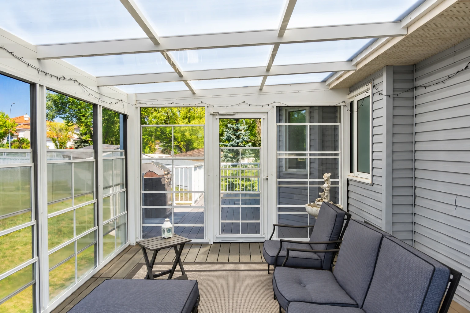 A three-season sunroom with a translucent roof, screened windows, and dark outdoor lounge seating.